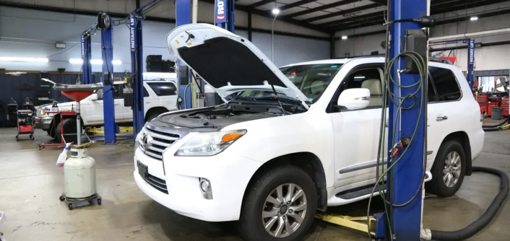 Japanese Motor Works: A white SUV with its hood open is on a hydraulic lift undergoing Lexus repair in a spacious car repair shop. Tools and equipment are visible in the well-lit background, alongside multiple vehicles, as part of their comprehensive Lexus care service.